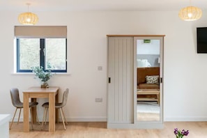 A room with a sliding door leading to a bed, a dining table with chairs, and a window with blinds.