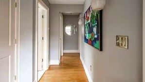A hallway with wooden flooring, a round mirror, and a colorful abstract painting on the wall. - Sunny House, By The Beach, Minutes From Portland (South Portland)
