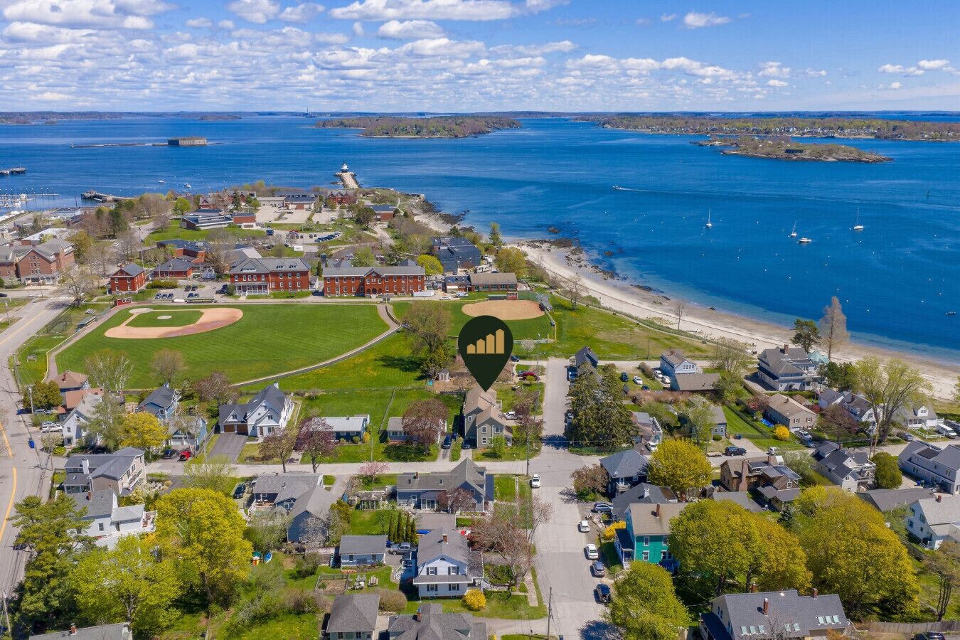 Luftaufnahme einer Küstenstadt mit einem Baseballfeld, Wohnhäusern und einem Leuchtturm.