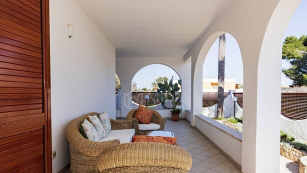 A covered outdoor seating area with wicker furniture, a potted plant, and a view of the surrounding buildings. - SALENTINE DAYS - 1 (Torre Lapillo)
