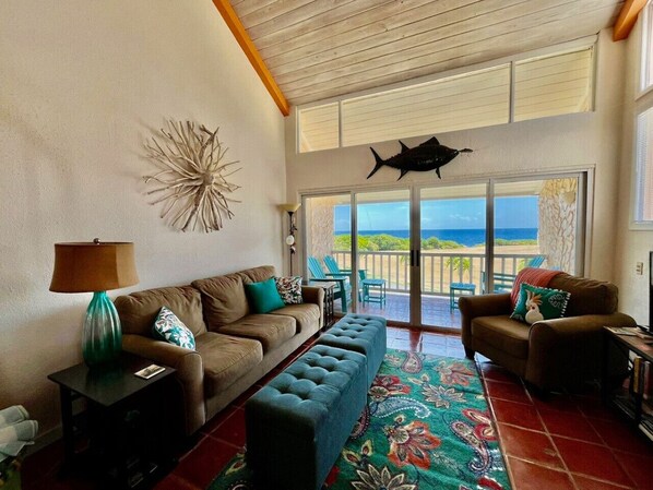A living room with a sofa, ottoman, and chairs, a lamp, and a decorative wall piece. - Villa Mango! at Gentle Winds (Christiansted)