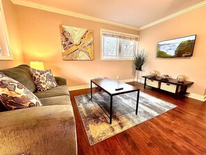 A living room with a sofa, coffee table, and a television on a wall. - Stylish Modern Apt Near Northside Hospital (Cumming)