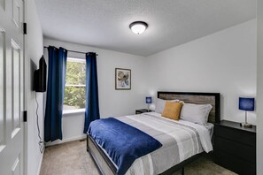 Un dormitorio con cama, lámparas de noche, una ventana con cortinas, un cuadro en la pared y una lámpara en el techo.