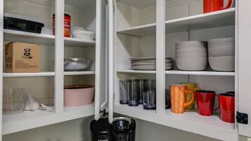 A kitchen with white cabinets, a coffee maker, and various kitchenware including bowls, plates, and mugs.