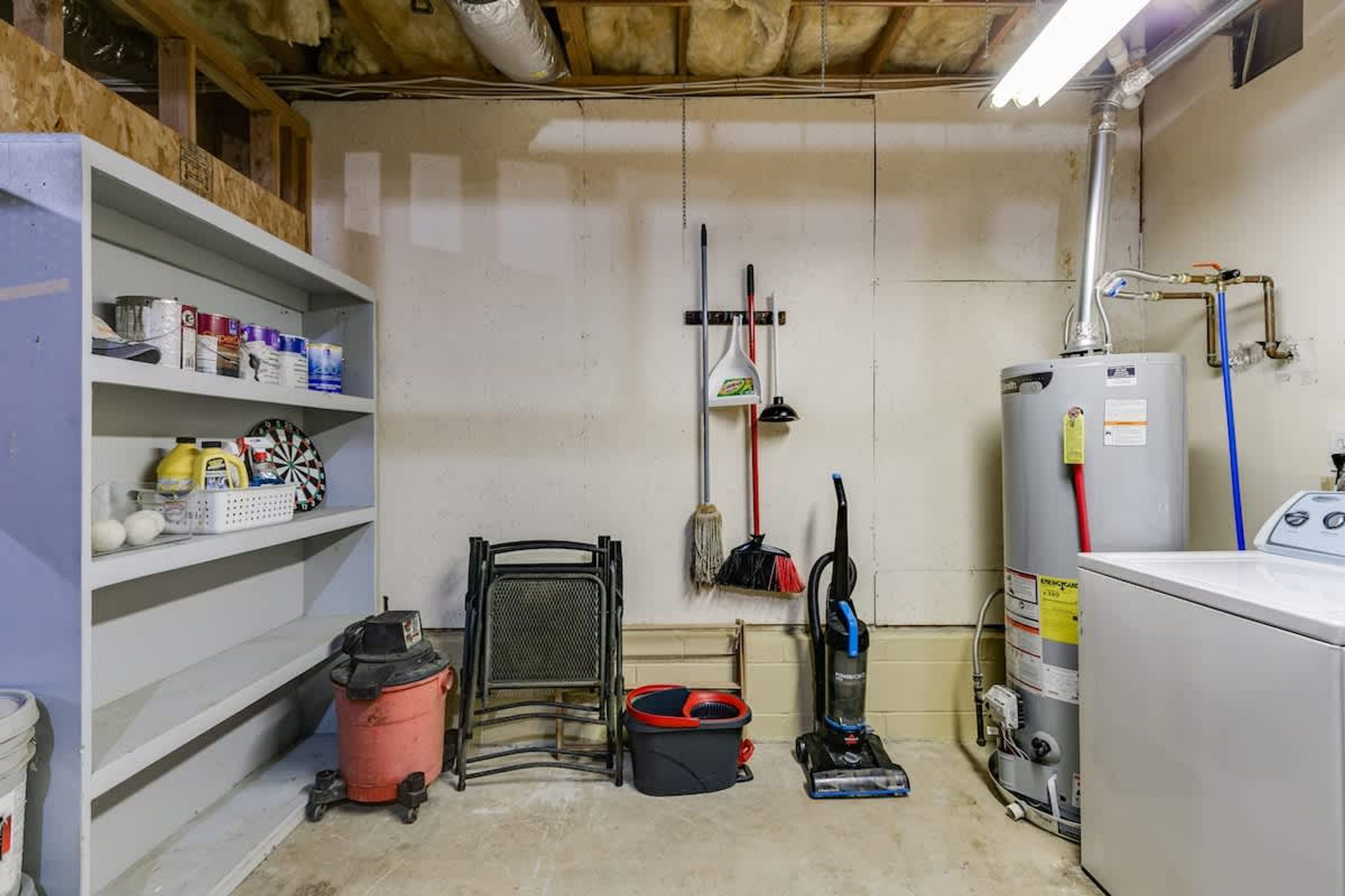 A laundry room with shelves, a vacuum cleaner, a water heater, and a washing machine.