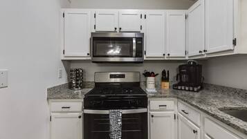 A kitchen with white cabinets, a stainless steel microwave, a black stove, and a coffee maker.