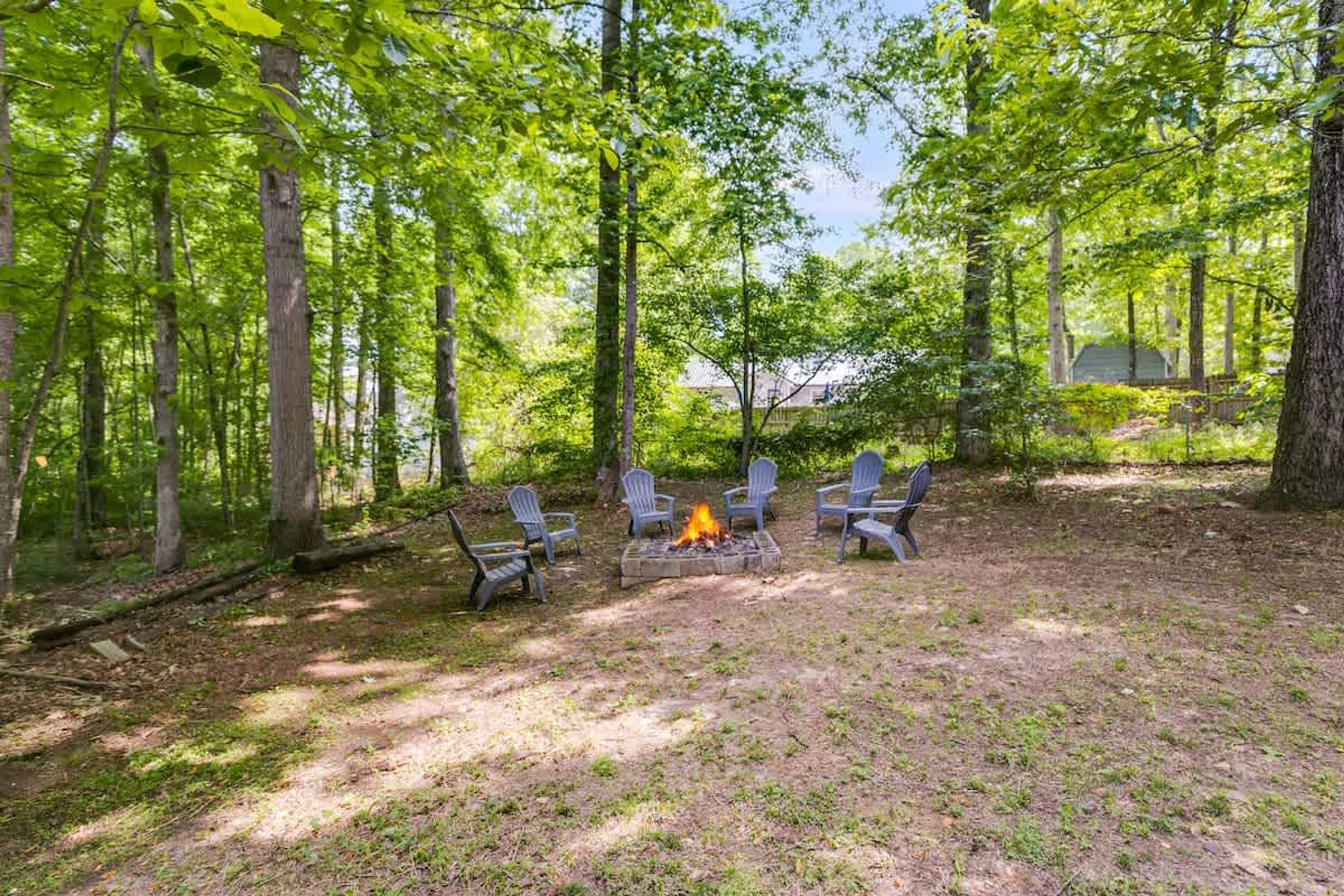 A forested campsite with a fire pit and chairs.