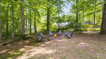 A forested campsite with a fire pit and chairs.