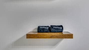 Un estante de madera con dos toallas azul oscuro etiquetadas 'Makeup' frente a una pared blanca lisa.