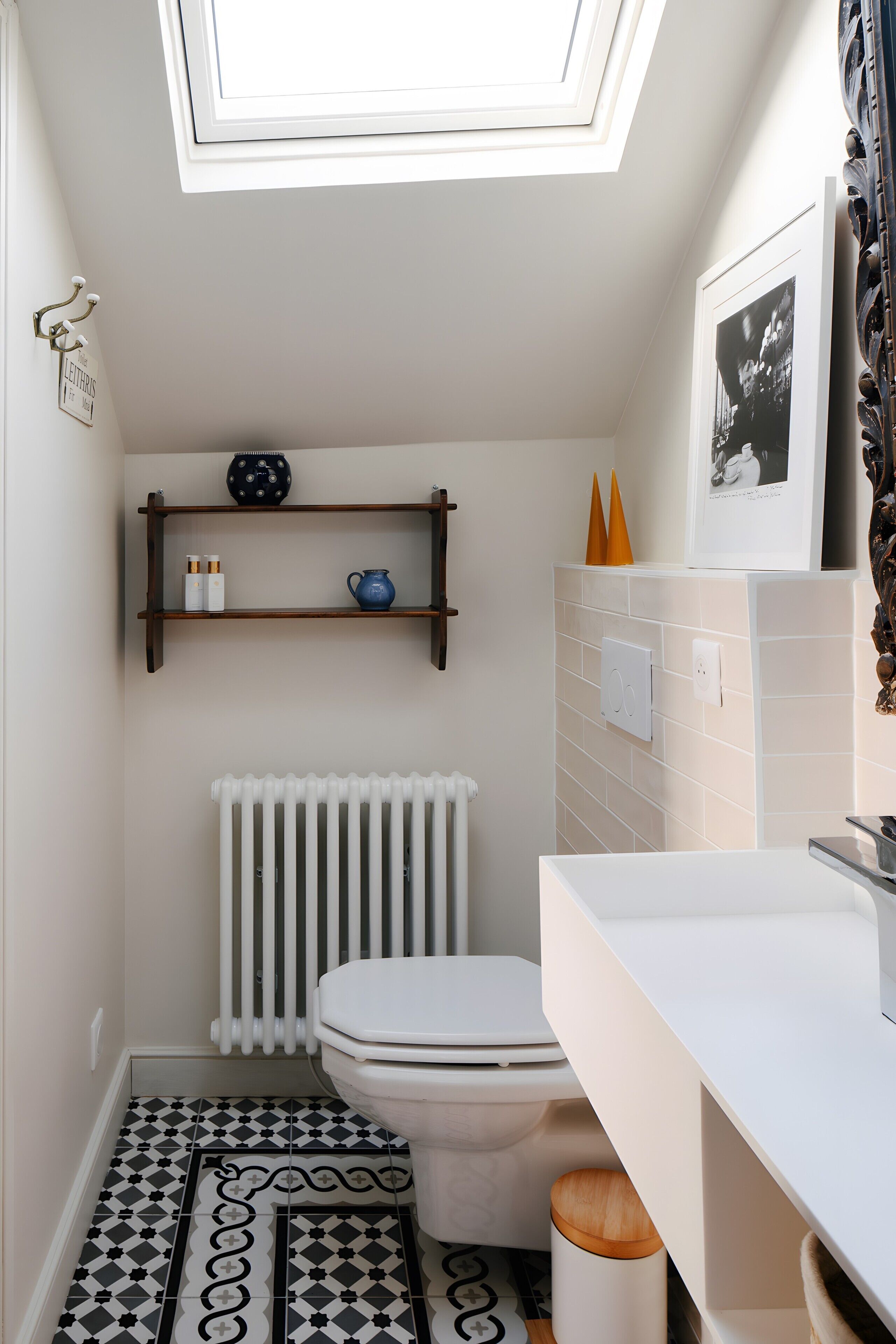 A compact bathroom with a skylight, a white radiator, a toilet, a shelf with toiletries, and a patterned floor.