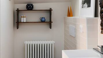 A compact bathroom with a skylight, a white radiator, a toilet, a shelf with toiletries, and a patterned floor.