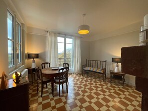 Un coin repas avec un sol à carreaux, une table ronde, des chaises, un banc et un luminaire suspendu.