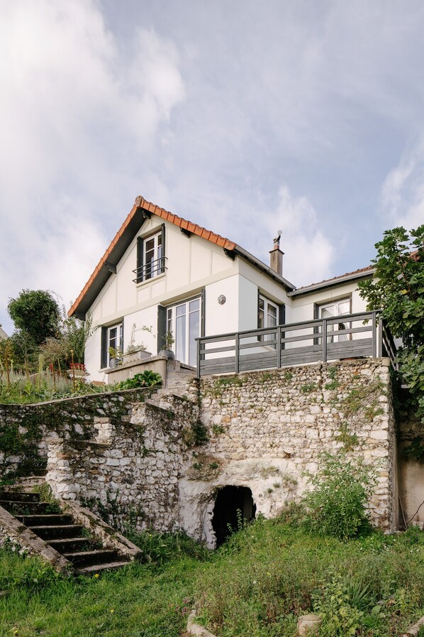 Una casa de dos pisos con una escalera de piedra que lleva a una terraza de madera.