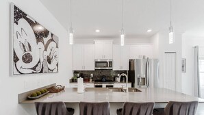 Una cocina moderna con armarios blancos, electrodomésticos de acero inoxidable y una isla central con taburetes de bar.