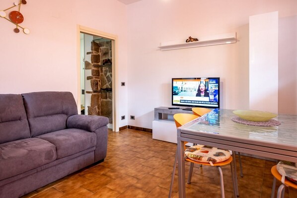 Una sala de estar con sofá, televisión, mesa de comedor y pared de piedra.