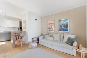 A modern living room with a sofa, a dining table with chairs, a kitchen area, and two framed pictures on the wall.
