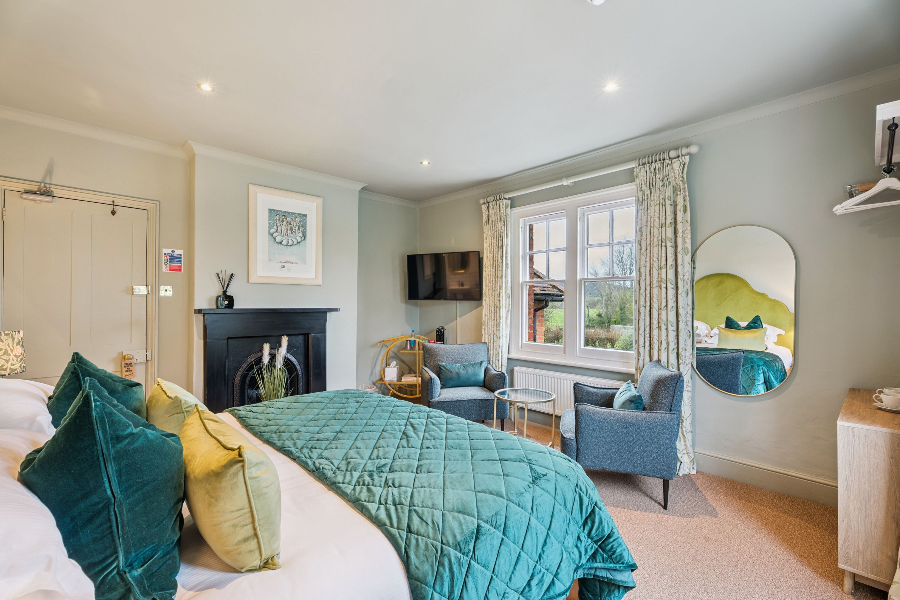 A bedroom with a bed, a chair, a small table, a fireplace, a TV, and a window with curtains.