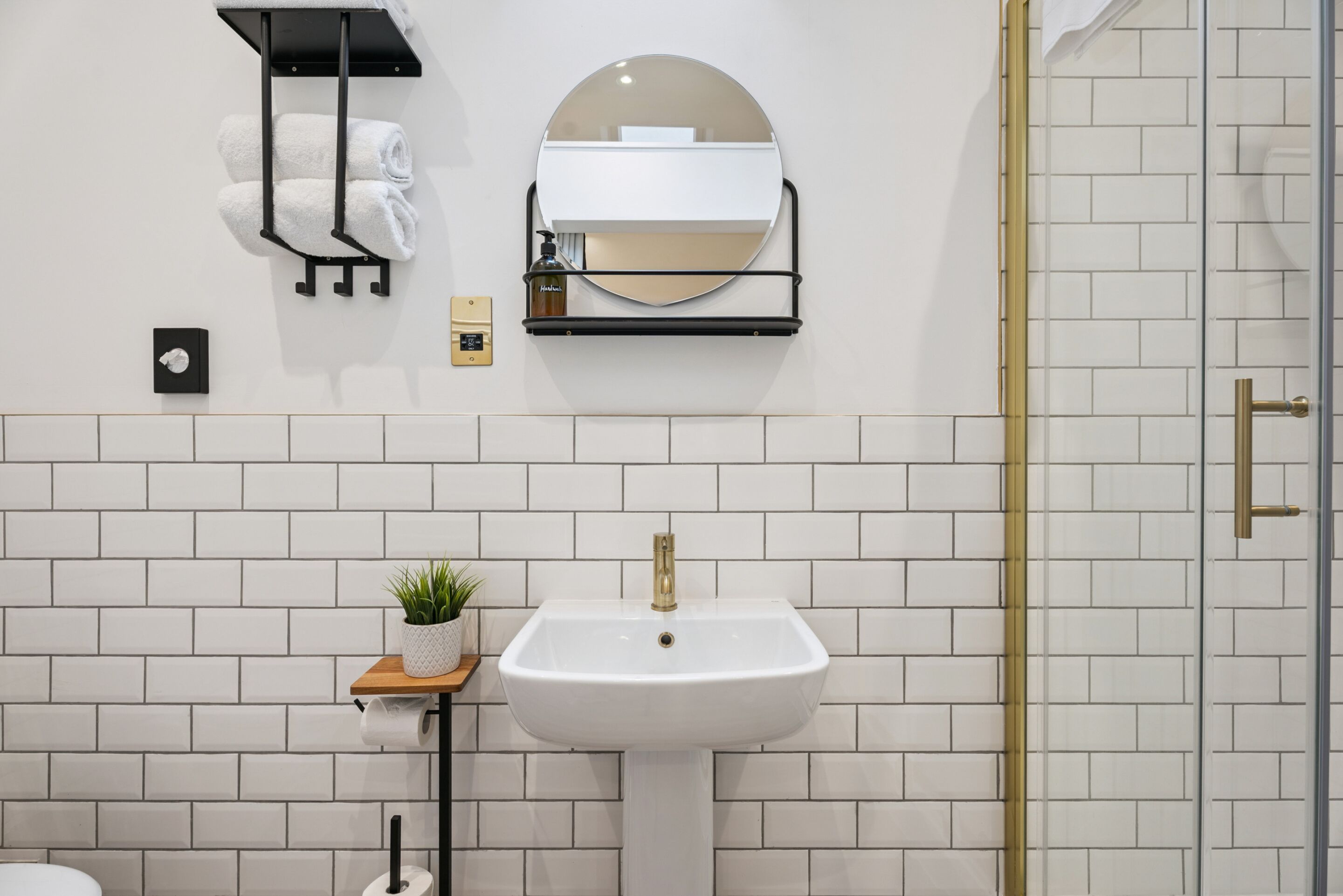 A bathroom with a white sink, a towel rack, a mirror, and a small plant.