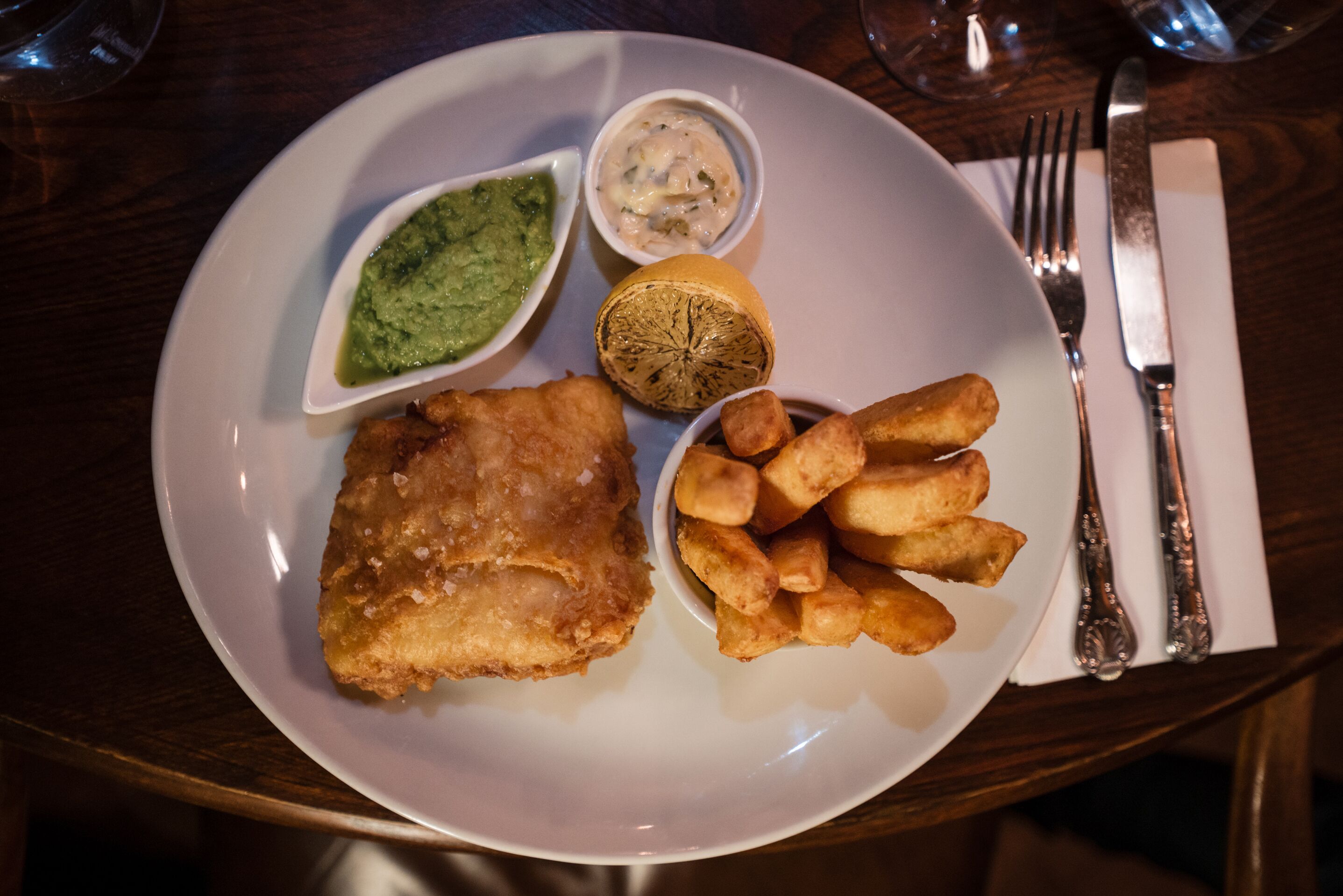 A plate with a piece of fried fish, a lemon, and a side of fries.