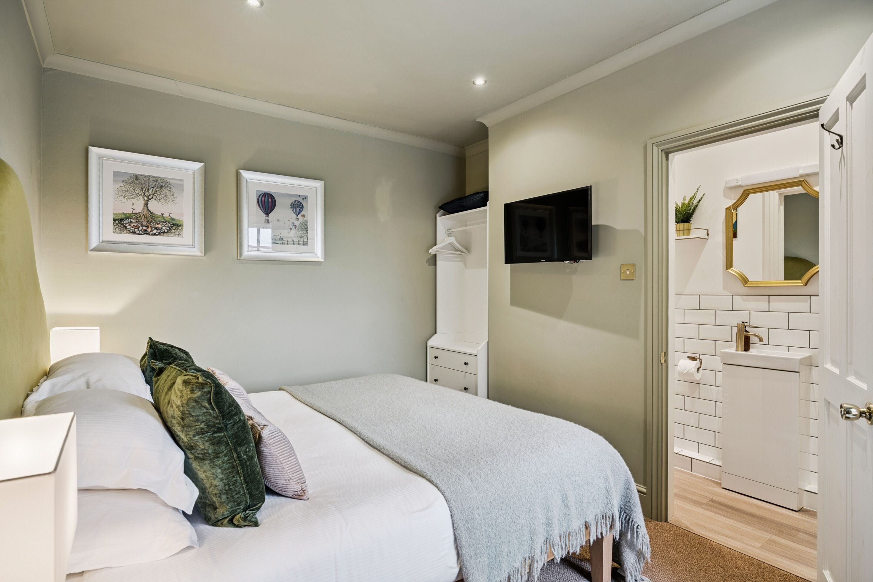 A bedroom with a bed, a TV mounted on the wall, a door with a mirror, and framed pictures on the wall.