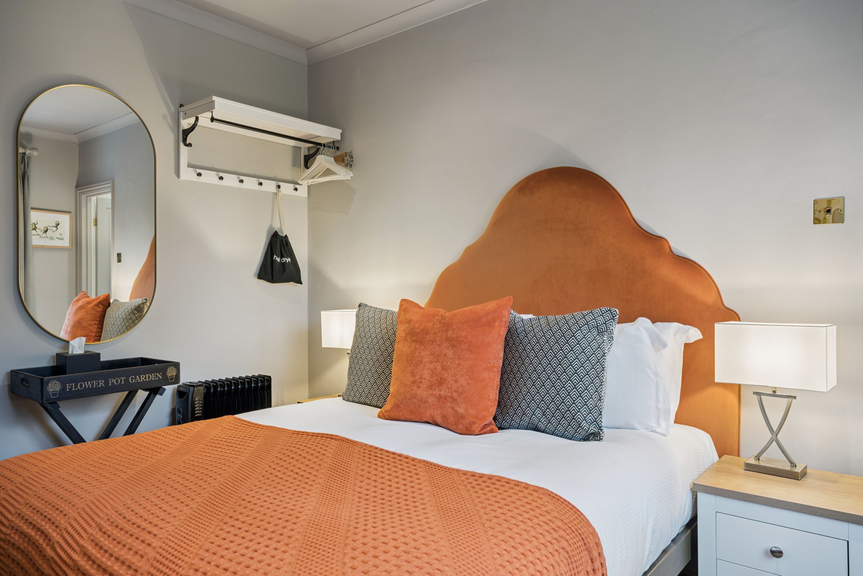 Hotelkamer met een groot bed, nachtkastje met lamp, spiegel, radiator en een wandplank met tas.