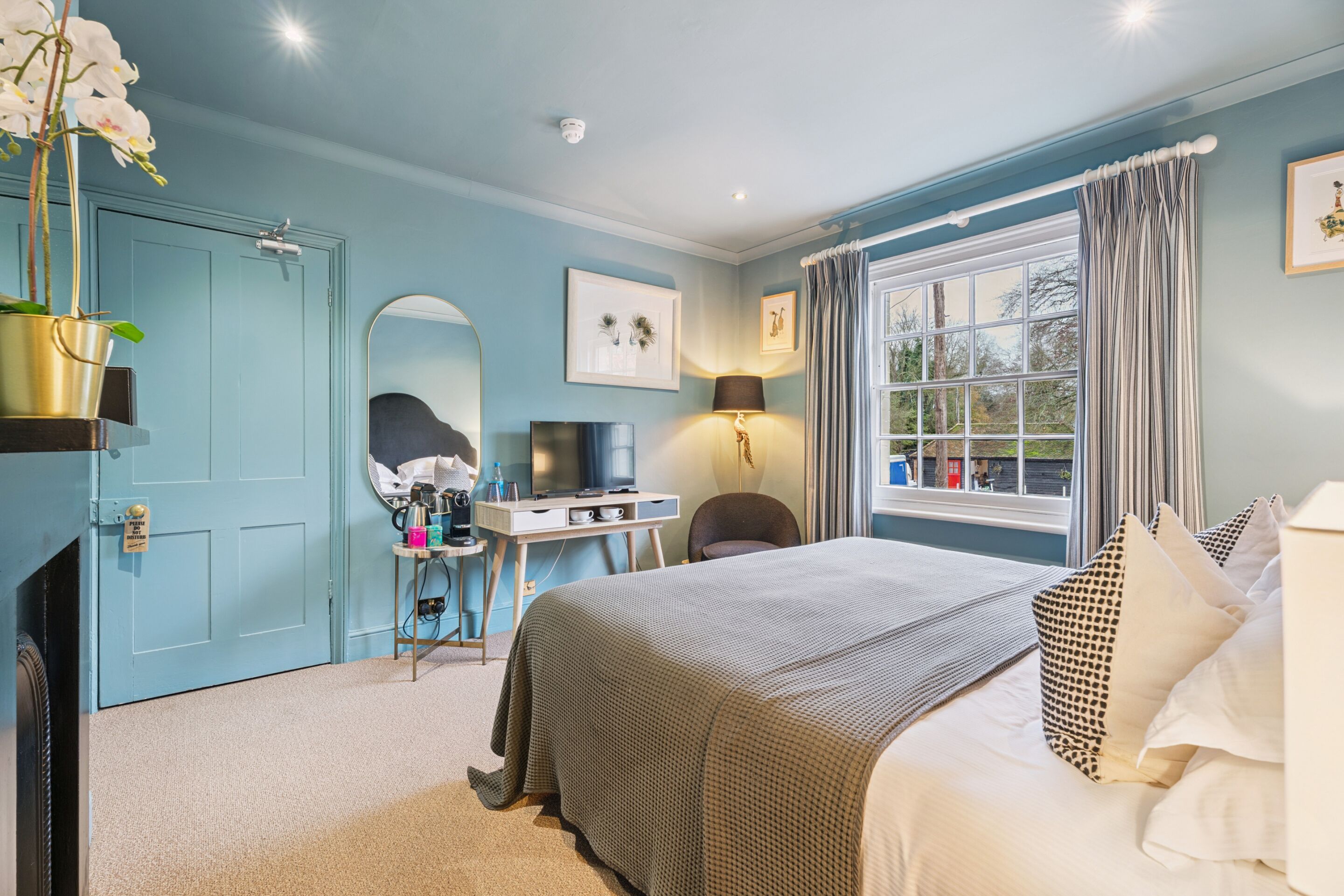 A bedroom with a bed, a desk, a chair, a TV, and a window with curtains.