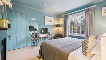 A bedroom with a bed, a desk, a chair, a TV, and a window with curtains.