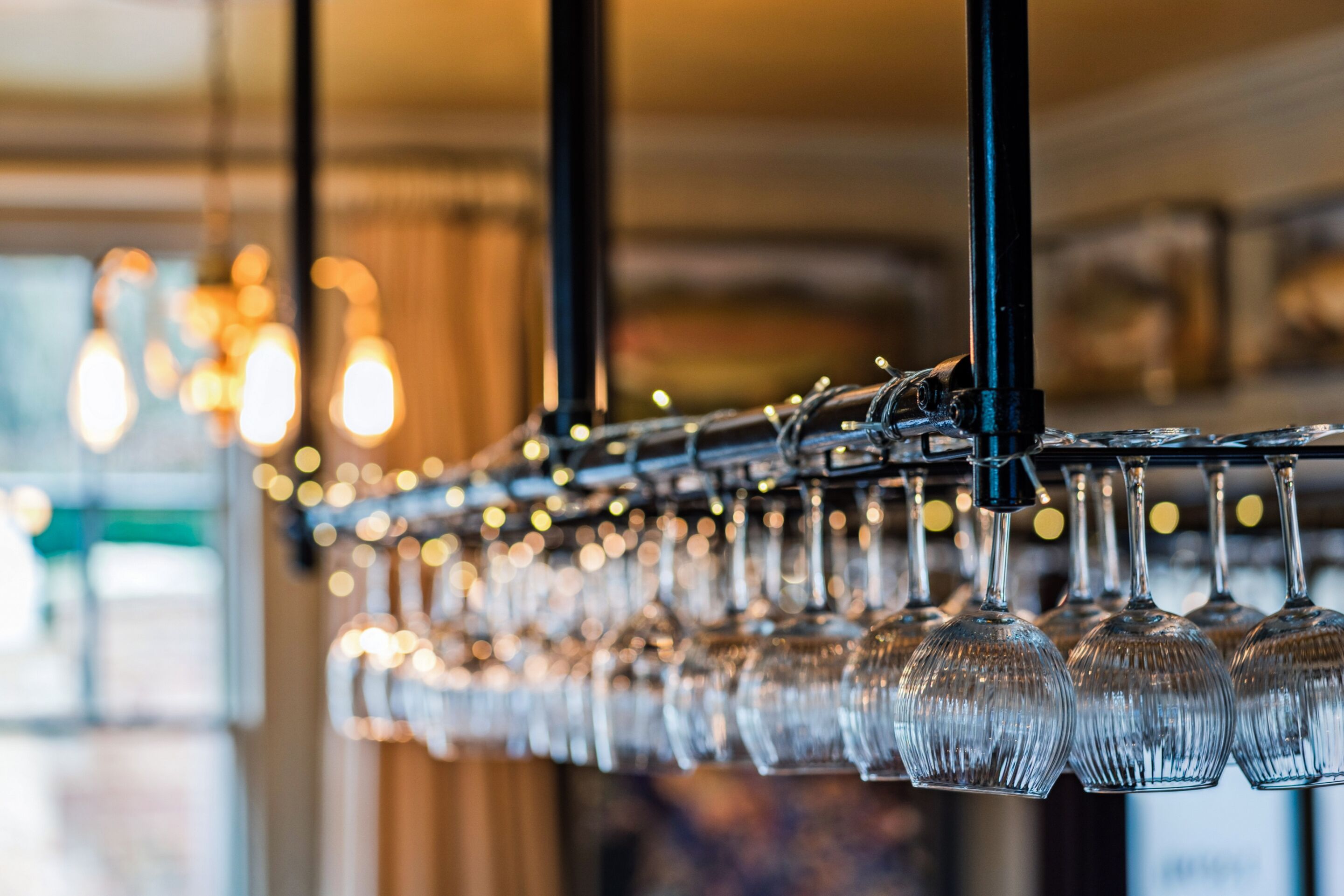 A row of clear wine glasses hanging from a black metal bar.