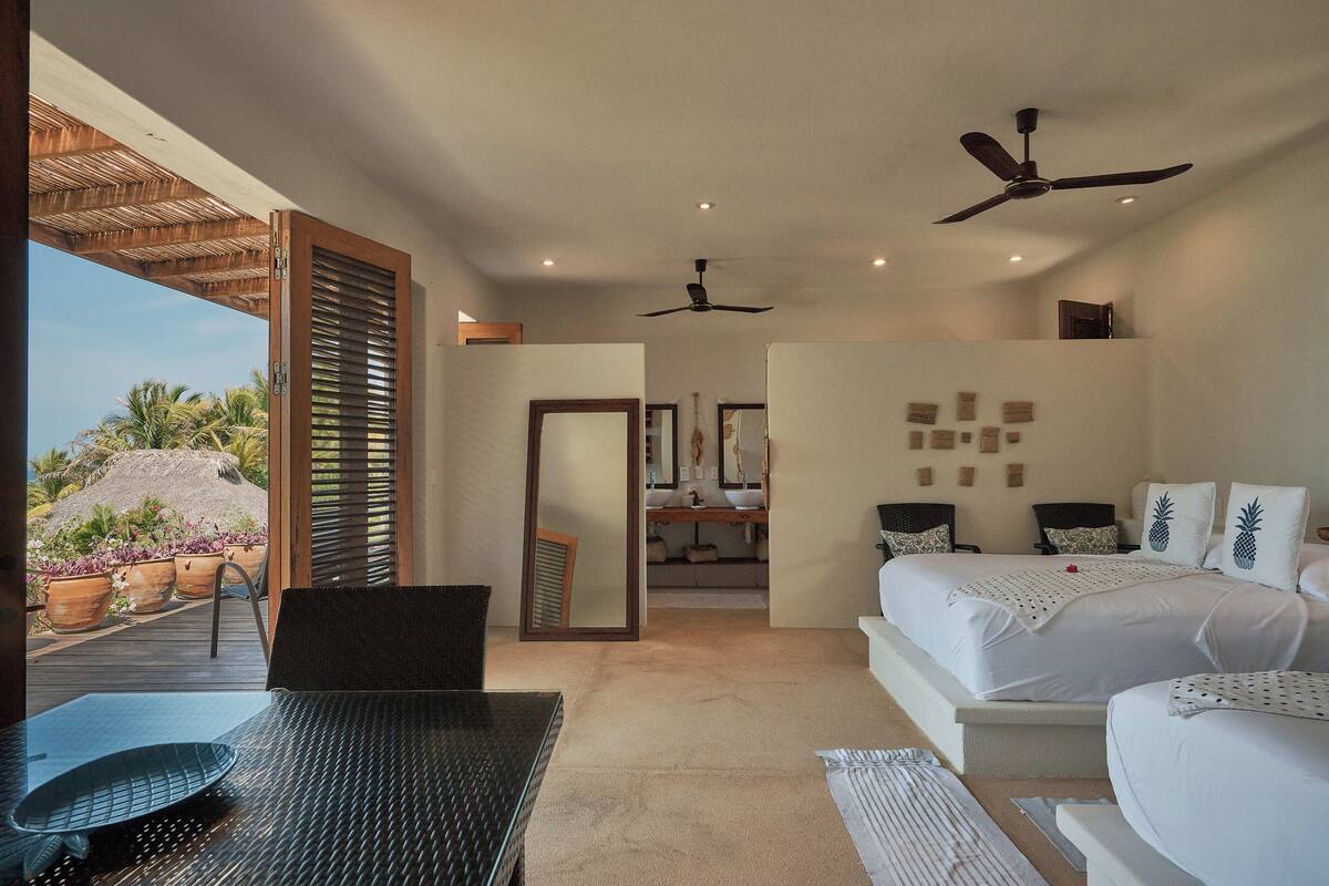 A bedroom with a bed, ceiling fans, a bathroom, and a view of the outdoors.