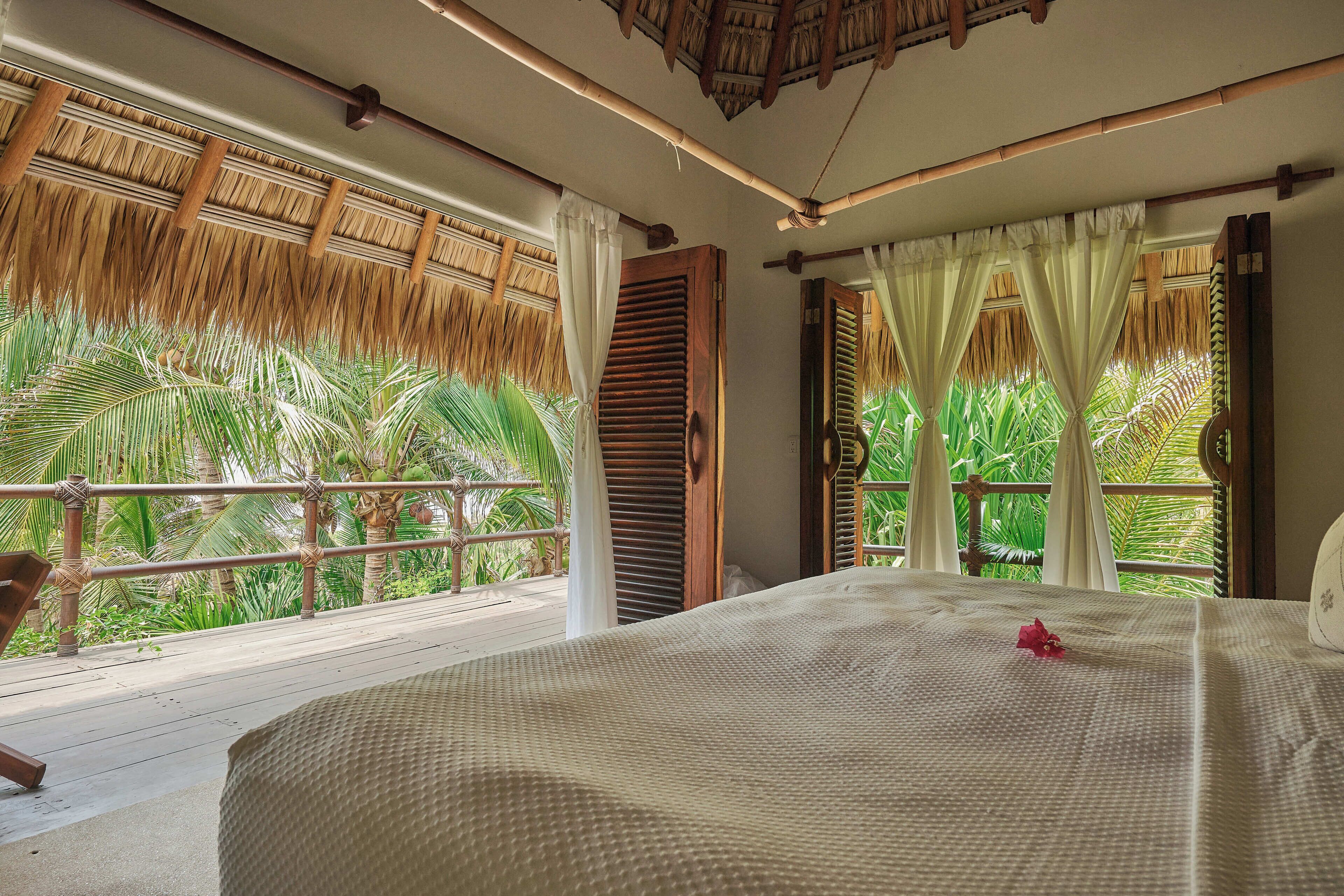 Un dormitorio con una cama grande, vistas a palmeras y un balcón con barandilla de madera.