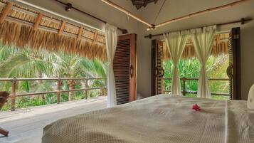Un dormitorio con una cama grande, vistas a palmeras y un balcón con barandilla de madera.