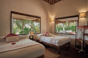 A room with two beds, a fan, a nightstand, and a view of palm trees. - Los Guajes Bungalows (Santa Maria Colotepec)