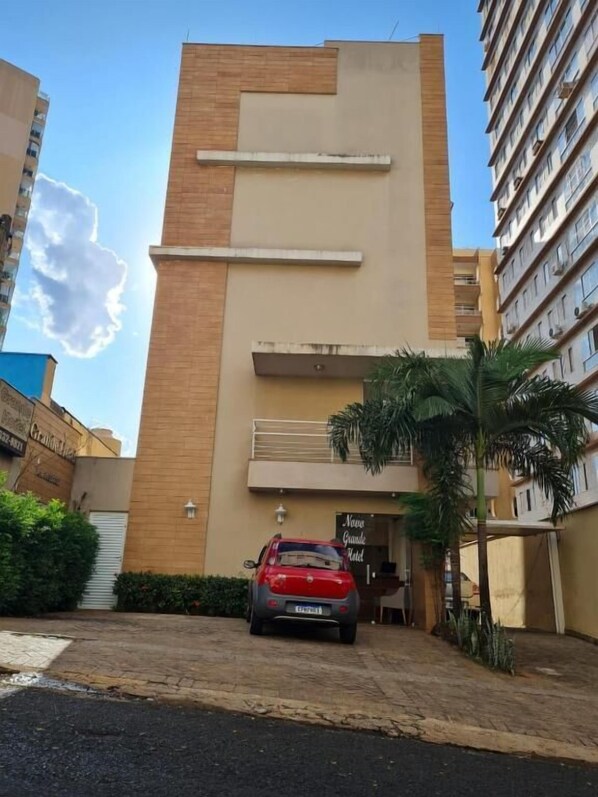 Un bâtiment moderne avec une voiture garée devant, un palmier et un ciel dégagé.