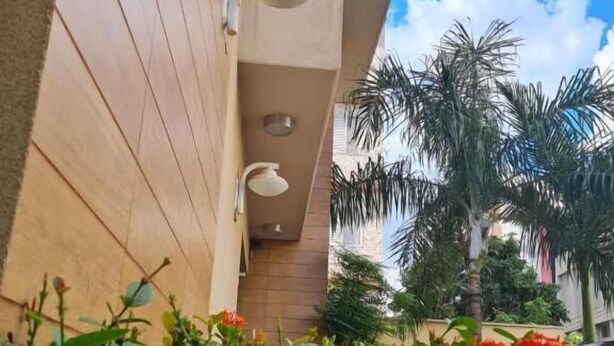 A building with a wooden exterior, a white exterior wall, a small balcony with a white chair, and a red car parked in the background. - novo grande hotel  (Ribeirão Preto)