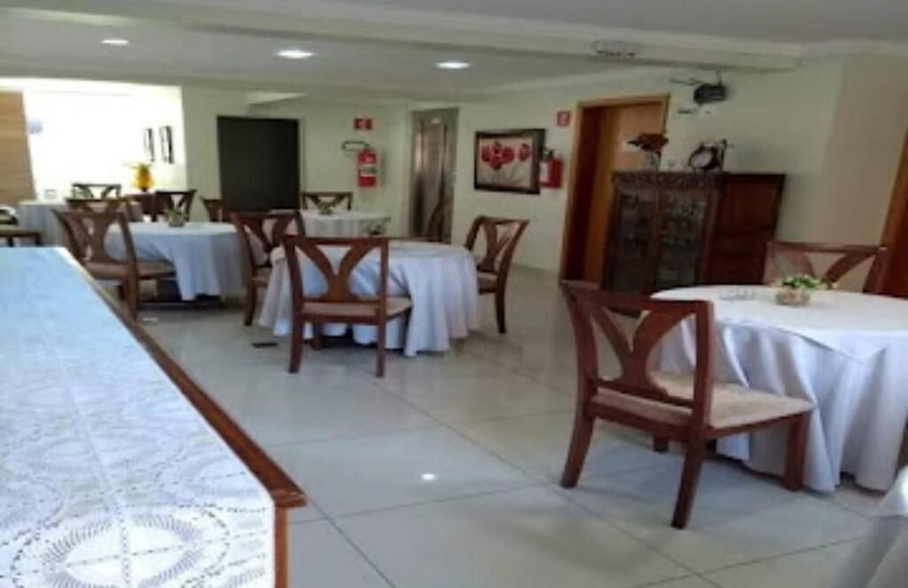 Un comedor con varias mesas y sillas, una mesa larga con mantel estampado y una puerta que da a otra habitación.