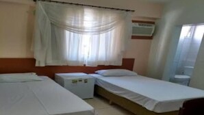 A room with two beds, a small table, a nightstand, and a window with sheer curtains. - novo grande hotel  (Ribeirão Preto)
