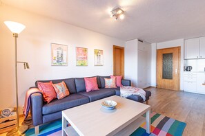 Ein modernes Wohnzimmer mit einer Couch, einem Couchtisch und einem durchgehenden Durchgang zur Küche.