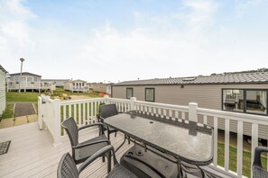 A deck with outdoor furniture, a white railing, and a view of mobile homes in the background. - Cabin Sleeps 8 - Pools, Parking, Pets (Weymouth)