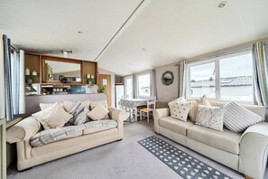 A modern living room with two sofas, a dining table, and a kitchen area. - Cabin Sleeps 8 - Pools, Parking, Pets (Weymouth)