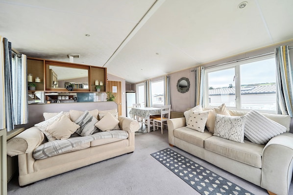 A modern living room with two sofas, a dining table, and a kitchen area. - Cabin Sleeps 8 - Pools, Parking, Pets (Weymouth)
