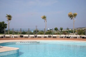 A swimming pool with lounge chairs and palm trees, surrounded by a fence. - Cabin Sleeps 8 - Pools, Parking, Pets (Weymouth)