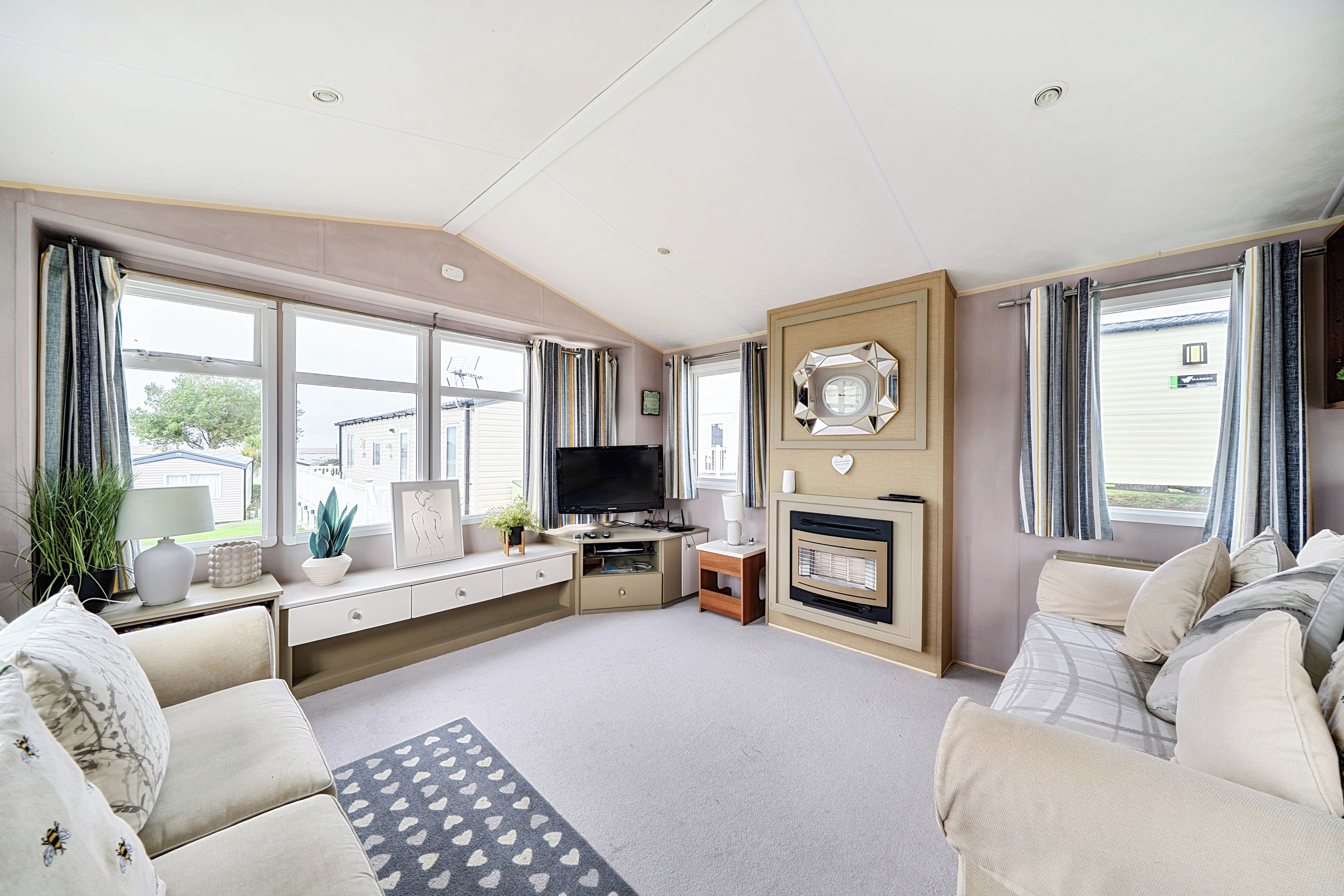 A living room with a sofa set, a television, a fireplace, and a large window.
