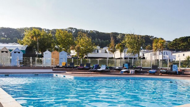Una piscina con sillones de descanso y vistas a casas y árboles al fondo.