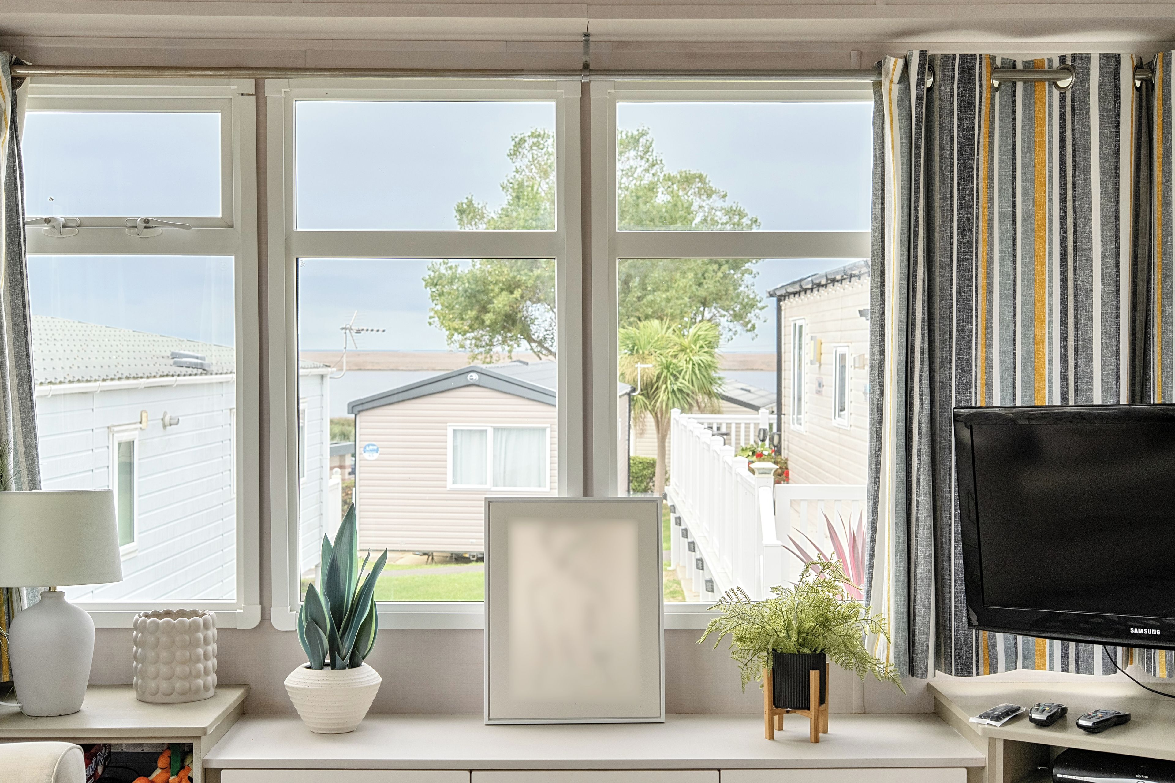 A room with a large window, a television, and a desk with a lamp and decorative items.