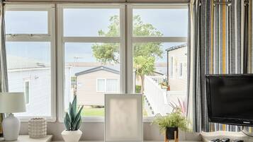 A room with a large window, a television, and a desk with a lamp and decorative items.