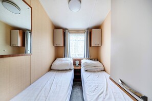 A narrow corridor leading to a bedroom with two single beds, a window with curtains, and a mirror on the left wall. - Cabin Sleeps 8 - Pools, Parking, Pets (Weymouth)