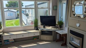 Una habitación con un ventanal grande, televisión, chimenea y escritorio con espacio de almacenamiento.