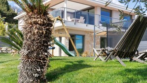 Una casa moderna de dos pisos con balcón, una palmera y un columpio.