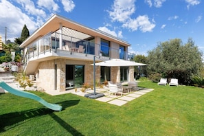 A modern two-story house with a balcony, a patio with outdoor furniture, and a small slide in the yard. - 🌿 Large Family Villa | Pool & Jacuzzi (Mougins)
