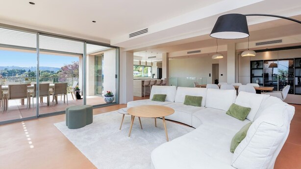 Una sala moderna con un sofá blanco, una mesa redonda y un comedor con una cocina al fondo.